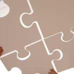 Hands of diverse individuals holding large puzzle pieces, symbolizing teamwork and unity.